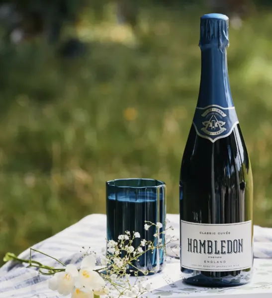 Hambledon Classic Cuvée sparkling wine bottle with blue glass and white flowers on outdoor table