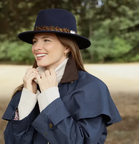 Smiling woman in navy blue hat and jacket, hands near collar, outdoor setting