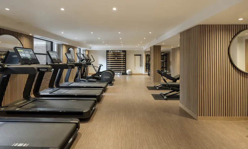 Modern hotel gym with rows of treadmills, weight benches, and wood-paneled walls with round mirrors