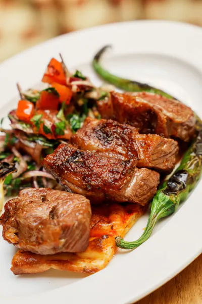 Grilled lamb chops with charred green peppers and tomato salad on a white plate