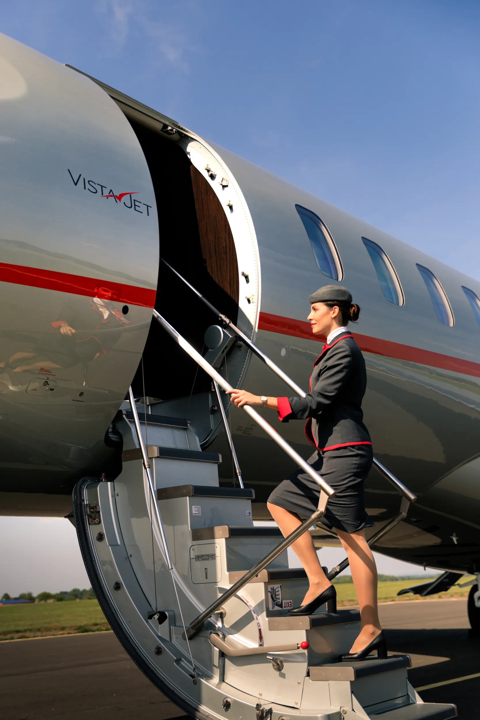 Flight attendant in dark uniform descending the stairs of a silver VistaJet private plane on the tarmac