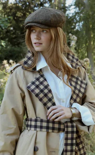 Woman in beige trench coat with checkered lining and brown flat cap, looking to the side outdoors