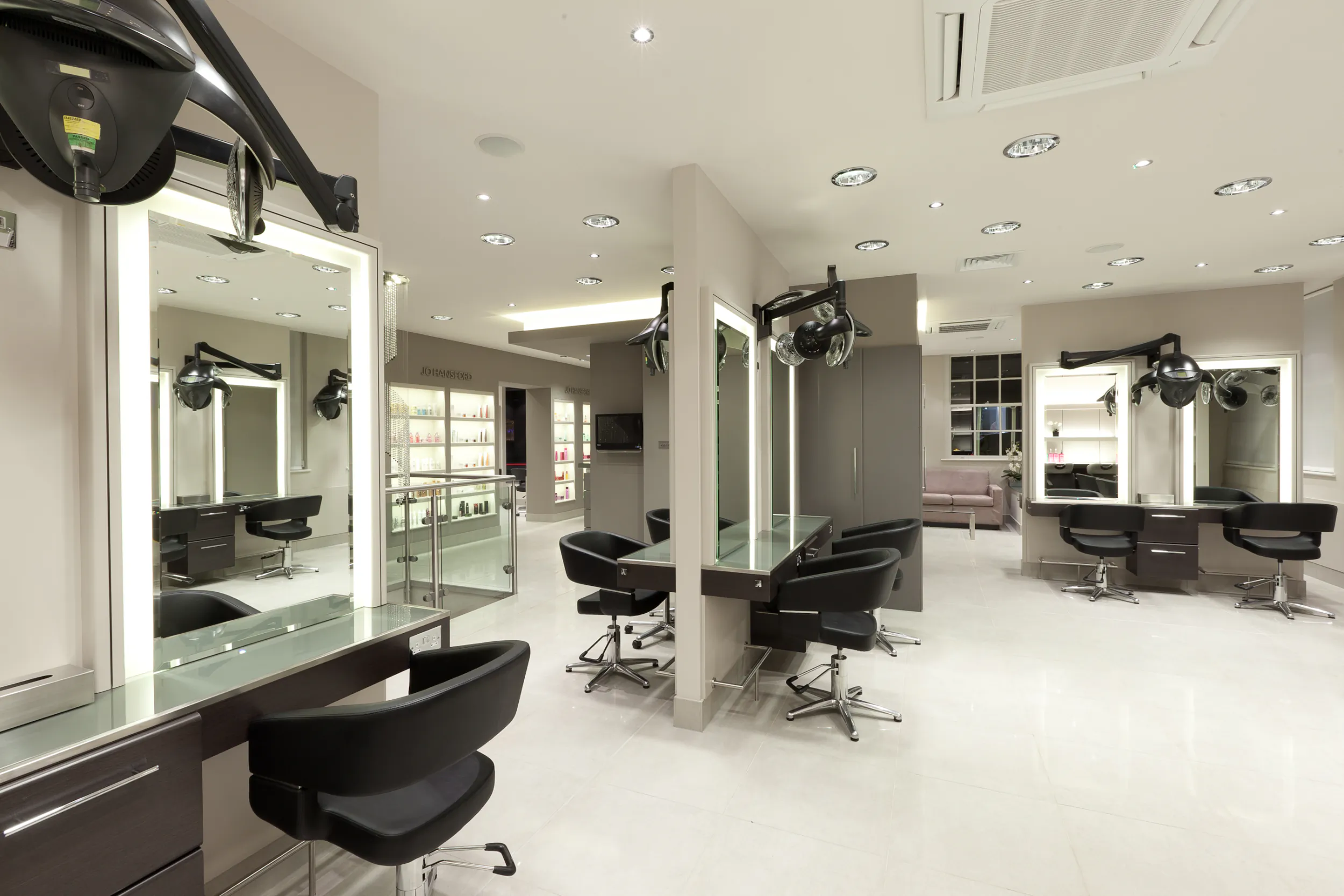 Modern hair salon interior with black styling chairs, illuminated mirrors, and sleek grey stations in a bright, spacious studio